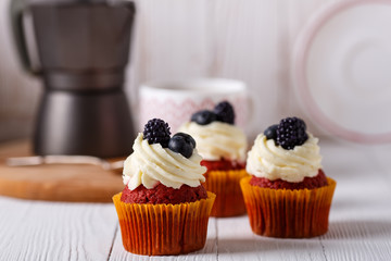 Tasty red velvet cupcakes on wooden table. Geyser coffee maker.