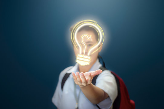 Young boy giving an idea. Student showing a light bulb to present an idea. Young school boy in school uniform visually presenting a light bulb to give an idea. Isolated blue background.