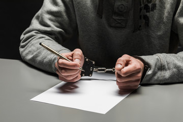 Hands of the criminal in handcuffs write a handle on paper. Sincere confession, request, statement....