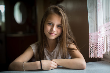Portrait of cute ten-year-old girl posing for the camera sitting at the table.