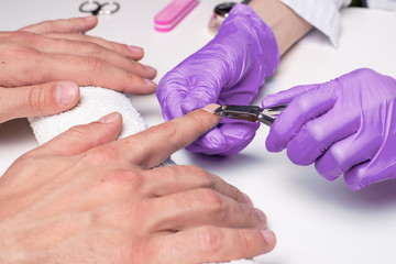 Men's manicure. Cosmetologist in rubber gloves cuts cuticles on men's hands