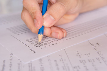 Students hand holding pencil writing selected choice on answer sheets and Mathematics question sheets. students testing doing examination. school exam