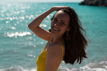 Large portrait in the hard light of the bright sun of a young woman on the sea in a yellow swimsuit, real life