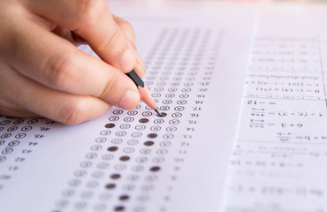 Obraz premium Students hand holding pencil writing selected choice on answer sheets and Mathematics question sheets. students testing doing examination. school exam