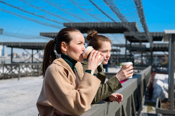 Two women talk on the waterfront with disposable cups of coffee. side view