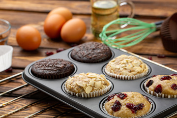 Different Muffins in bakeware or muffin pan on broun wooden background. Basic muffin recipe. Homemade muffins for breakfast or dessert.
