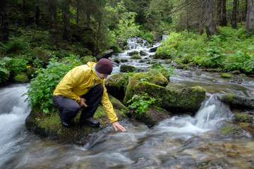 Man drink water from clear mountain stream in the lush forest. Wilderness scene