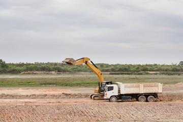 Yellow excavator machine loading soil into a dump truck at construction site