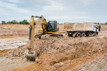 Obraz premium Yellow excavator machine loading soil into a dump truck at construction site