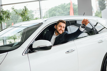 Man is holding a key of their new car, looking at camera and smiling.