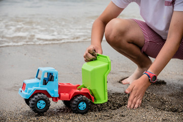 boy playing on the shore of the beach with a green, blue and red toy truck