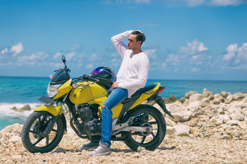 Fototapeta na wymiar Young handsome man sitting on motorcycle on the tropical beach.