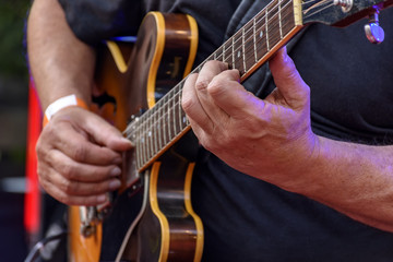 Detail of guitarist's hands and his black electric guitar at an outdoor jazz presentation