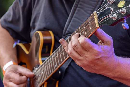 Detail of guitarist's hands and his black electric guitar at an outdoor jazz presentation