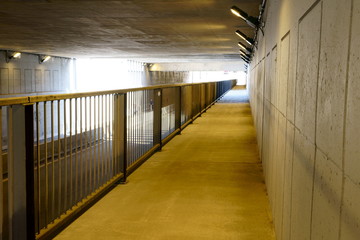 An empty underpass with nobody, made of concrete during the day, yellow lights opened.