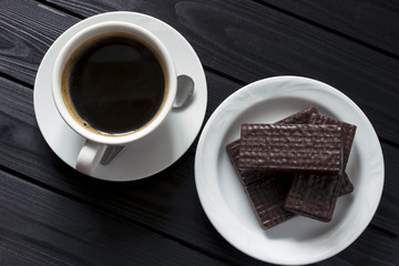 wafers in chocolate and a cup of coffee on a tree, a dark table, view from above