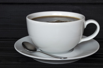 a cup of coffee in a plate with a spoon on a dark wooden background