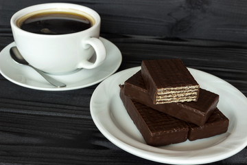 wafers in chocolate and a cup of coffee on a tree, a dark table