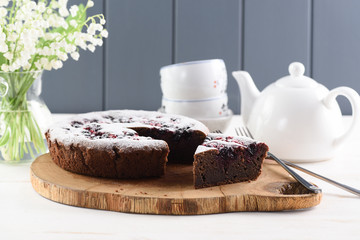 Healthy dessert. Traditional Siberian cake with bird cherry flour, cowberries and black currants served with white teaware and lily of the valley bouquet on oak board