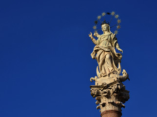 Fototapeta na wymiar Statue of Virgin Mary of the Stars crushing dragon and crescent at the top of an ancient column in the historic center of Lucca, erected in 1687 (with copy space)