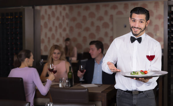 Young waiter with tray welcoming to restaurant