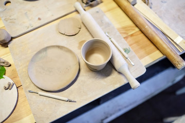 Earthenware. Ceramic products from raw clay. Mug, bowl, rolling pin lying on a wooden table. Art therapy lessons. Nerikomi technique
