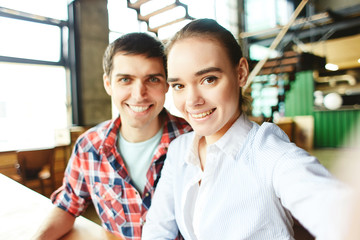 Fototapeta premium Pretty girl and handsome man posing at camera taking selfie and smiling happily sitting at table