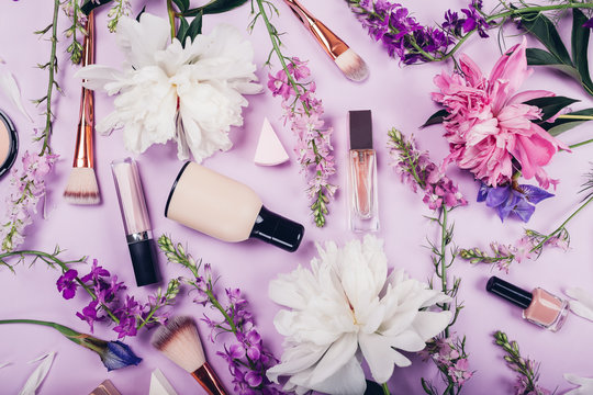 Set of cosmetics and brushes with fresh flowers on purple background. Organic cosmetics concept