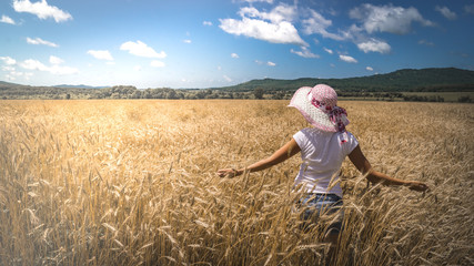 Girl In a hat walks the wheat field and strokes the ears of wheat.