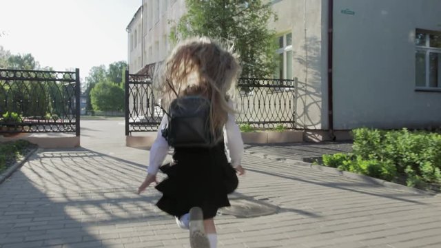 A little funny schoolgirl in school uniform and a briefcase on her shoulders runs to school. Steadicam shot