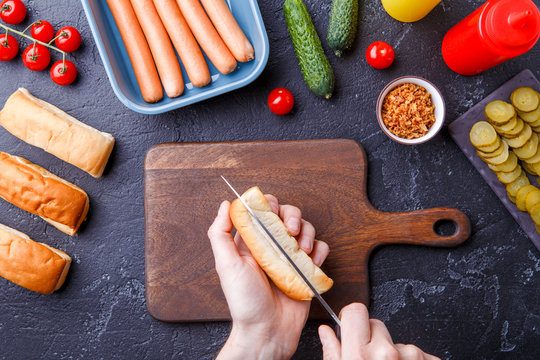 Photo on top of table with ingredients for hot dogs, cutting board, man's hands