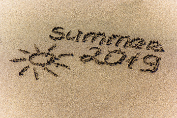 The word summer and sun written in the sand on a beach