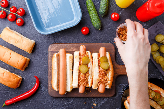 Picture from above of man doing hotdogs on cutting board on table with sausages