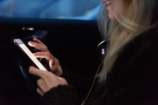 Crop smiling girl browsing smartphone in car