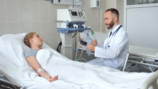 Doctor sitting near hospital bed and discussing with young female patient