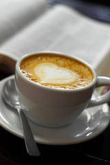 A cup of latte coffee on a tabletop next to a christian bible in spanish.