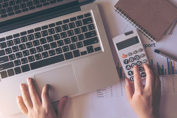 close up woman using calculator and laptop on paper graph data with doing finance at office. top view