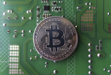 Silver souvenir coin Bitcoin on computer circuit board background.