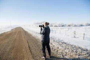a woman standing on a dirt road in the early morning hours on a winter day holding a camera