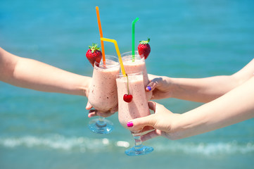 Three fruit juice smoothie in classic glass cups of berry fruits turquois sea water background. Three girls cheers
