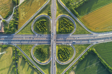 Cloverleaf interchange seen from above. Aerial view of highway road junction in the countryside with trees and cultivated fields. Bird's eye view. - 207992124