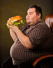 Diet failure of fat man eating fast food hamberger. Breakfast for overweight person who spoiled healthy food by eating huge hamburger. Junk meal leads to obesity. Use of harmful products. - 207992136