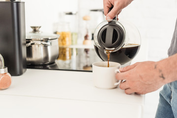 Fototapeta na wymiar partial view of man pouring coffee into cup from coffee maker at kitchen