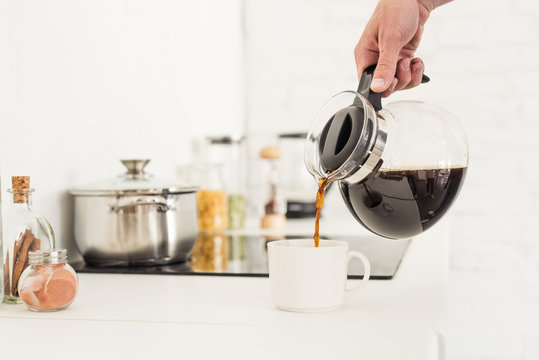 cropped image of man pouring coffee into cup from coffee maker at kitchen