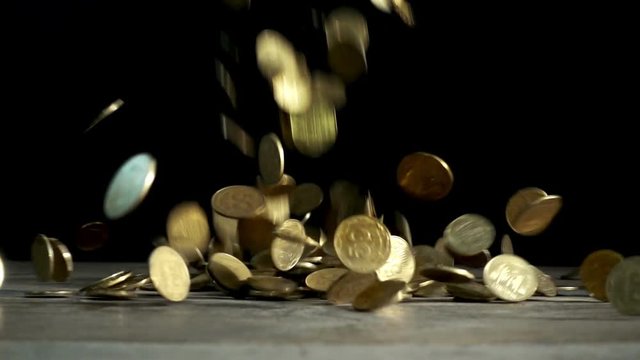 Slow motion, a pile of coins falls on a wooden table on a black background. Ukrainian coins are falling into a heap
