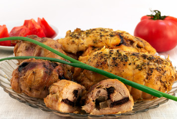 Meat dish from baked rolls with prunes, green onions and red tomatoes in the background.