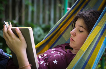 introvert teenager girl read book in hammock on summer outdoor green garden background