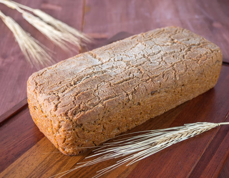 Homemade baked bread and a stalk of wheat on a cutting board