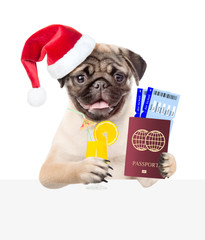 Dog in red christmas hat holds orange cocktail, airline tickets and passport above white banner. isolated on white background