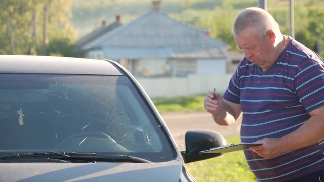 A man touches the crack on the front window, he considers the cost of repairs.